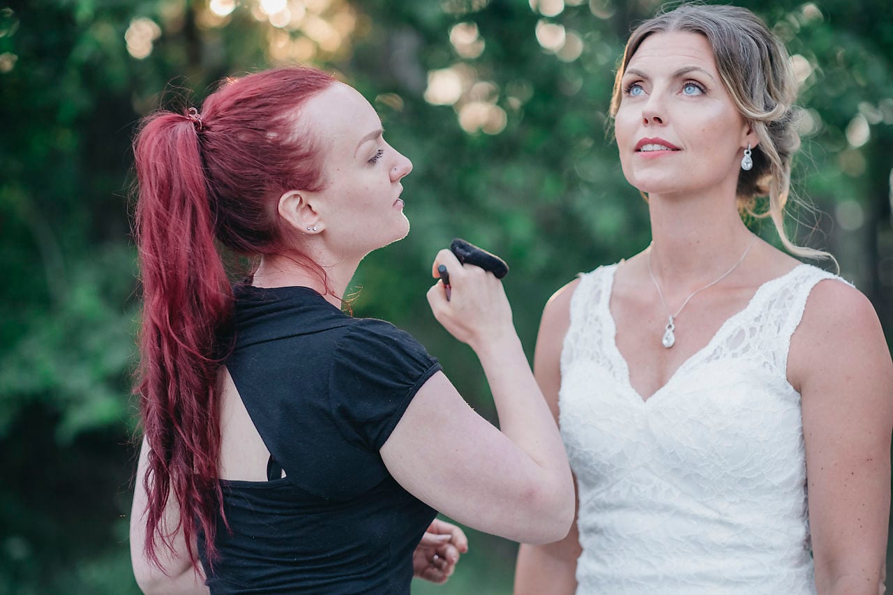 Makeupartist applicerar bröllopsmakeup på en brud utomhus.